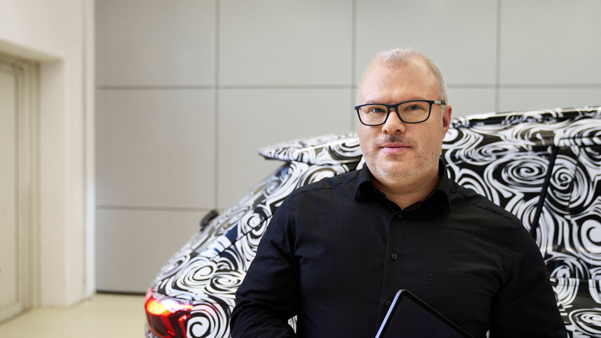 Steffen schaut in die Kamera und hat einen Audi hinter sich mit einem schwarz-weißen Muster