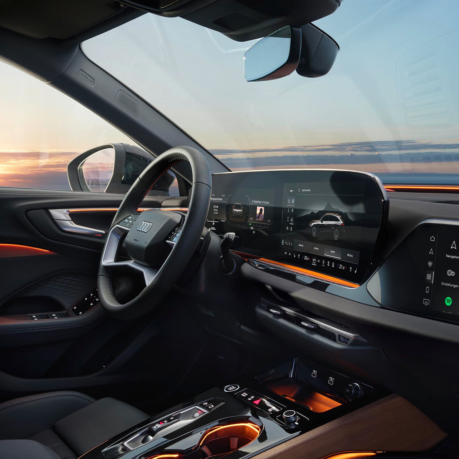 Innenraum eines Audi mit digitalem Cockpit, Ambiente-Beleuchtung und Blick auf Sonnenuntergang durch das Seitenfenster