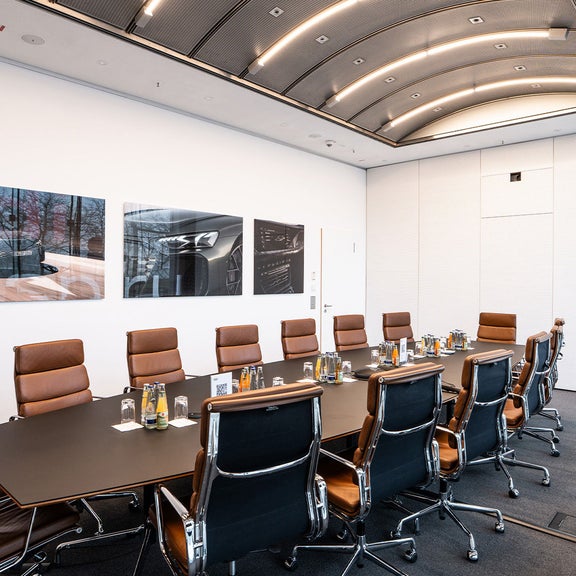 Konferenzraum mit langem Tisch, braunen Drehstühlen und Getränken auf dem Tisch.