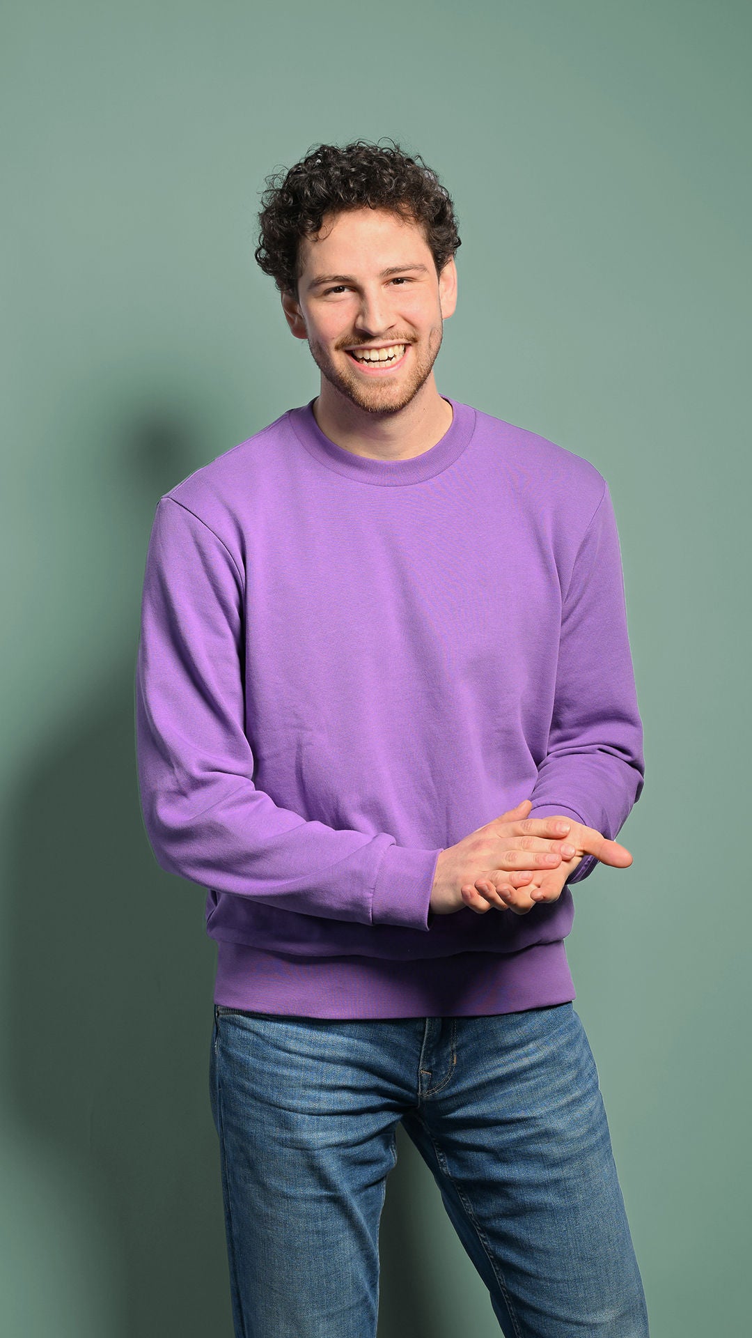 Fabian schaut in die Kamera und lacht mit gefalteten Händen 