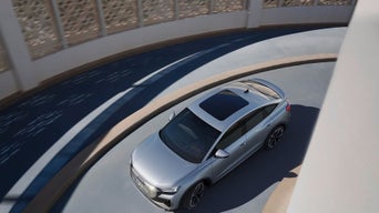 A silver Audi Q4 Sportback e-tron navigates a modern, curved ramp with intricate architectural details in the background.