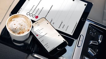 Ein Kaffee, Tablet und Handy liegen auf der Mittelkonsole im Auto