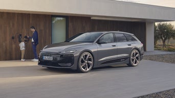 A6 Avant e-tron sett fra siden foran et moderne hus. En vegglader er montert på husveggen, der en far står sammen med et barn.