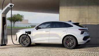 A white Q3 Sportback e-hybrid parked in front of an urban building is charging at a public charging station.