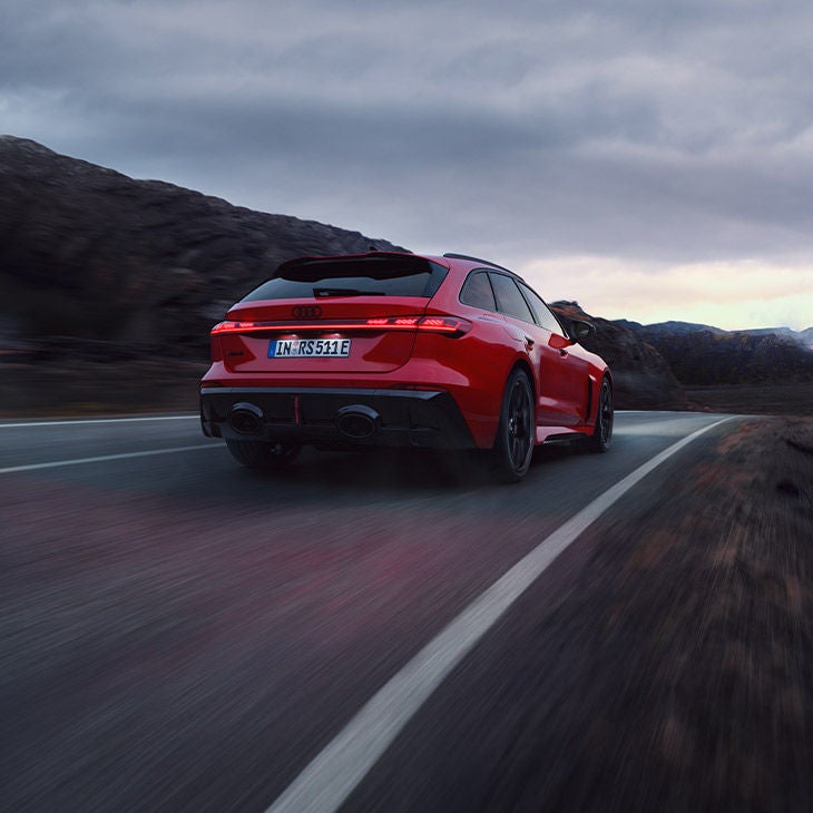 Vue arrière d'une Audi RS 5 Avant rouge circulant sur une route de montagne sinueuse.