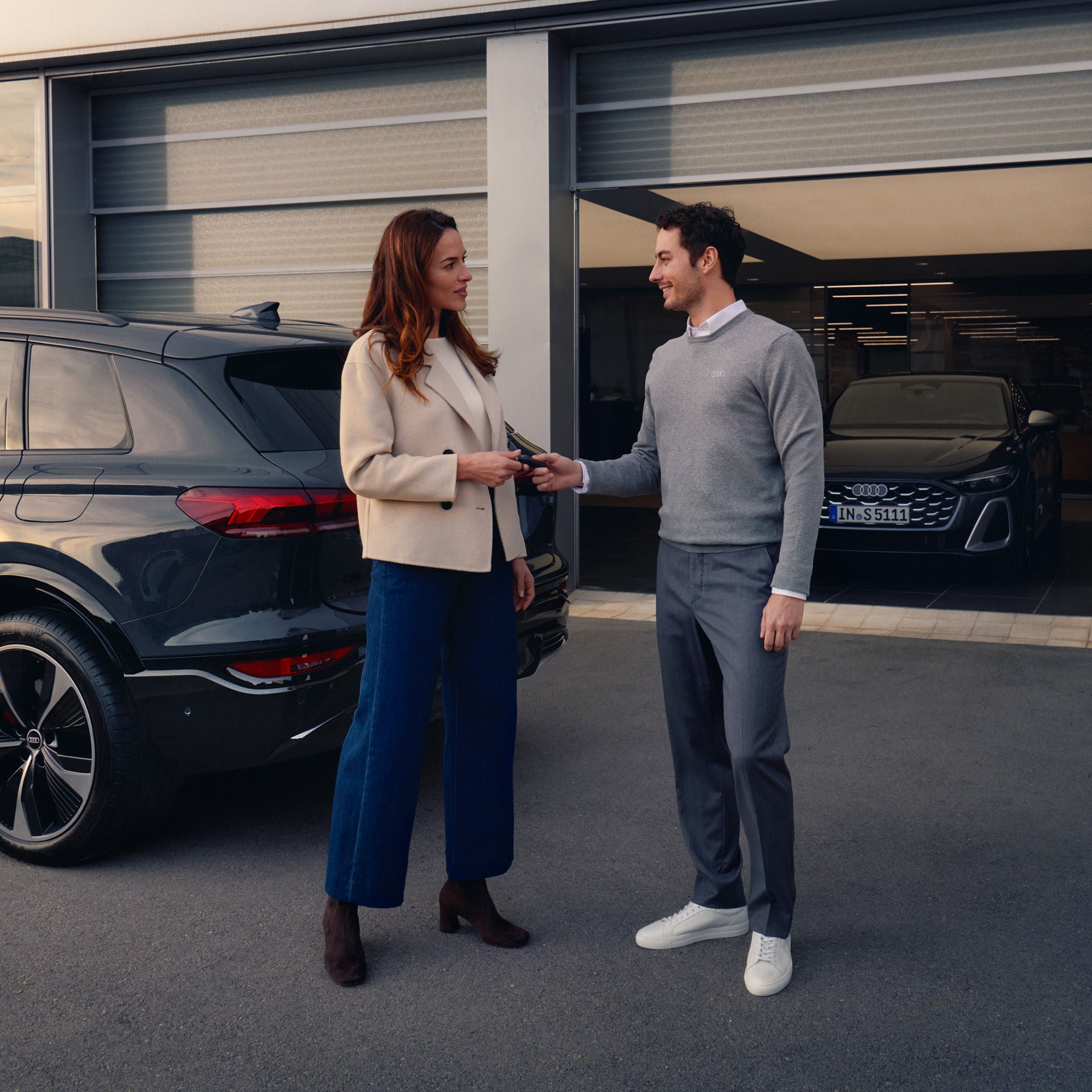 Frau und Mann übergeben sich vor einem Autohaus die Autoschlüssel neben einem schwarzen SUV.