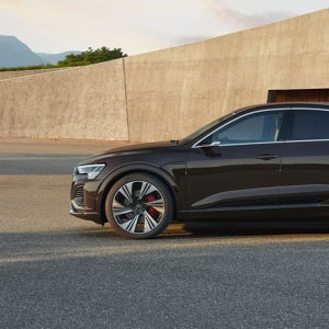 A black Audi car parked on an asphalt lot with a modern concrete building in the background. The scene conveys a sense of luxury and sophistication.