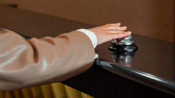 Hand drückt auf eine silberne Serviceklingel auf einem dunklen Tresen.