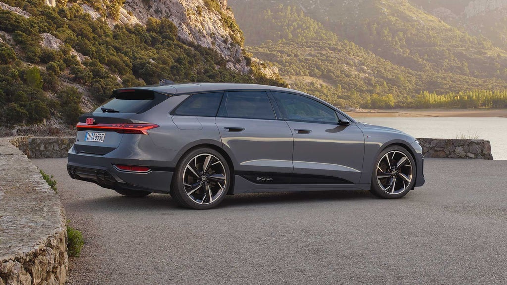 Grauer Audi A6 Avant e-tron seitlich auf Parkplatz vor See und bewaldeten Bergen.