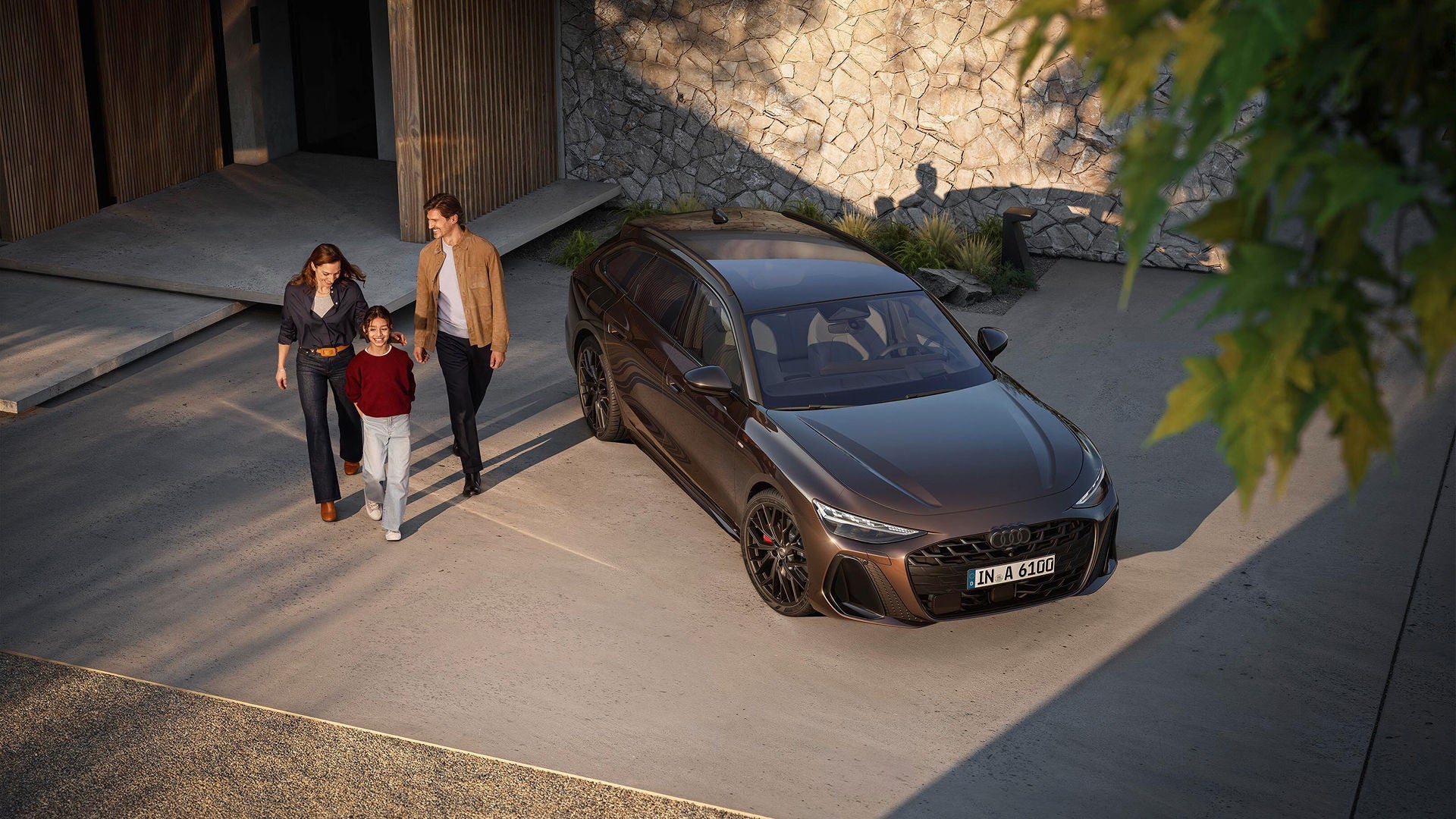 A family of three walks happily beside a sleek, brown parked Audi in a modern driveway. 