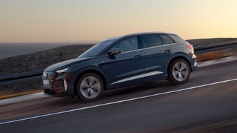 Zijaanzicht van de Audi Q4 SUV e-tron die in de schemering een hellende weg afrijdt. Op de achtergrond is de zee te zien.