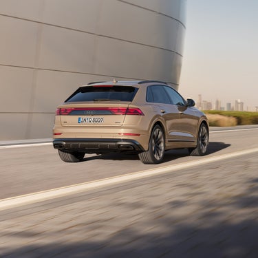 Ein goldener Audi Q8 SUV fährt auf einer Straße, die Heckansicht zeigt dynamische Bewegung.