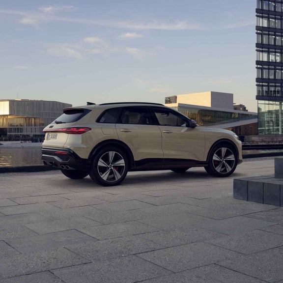 The beige Edition One of the SQ5 SUV with accents in Mythos Black. Glass building facades can be seen in the background.