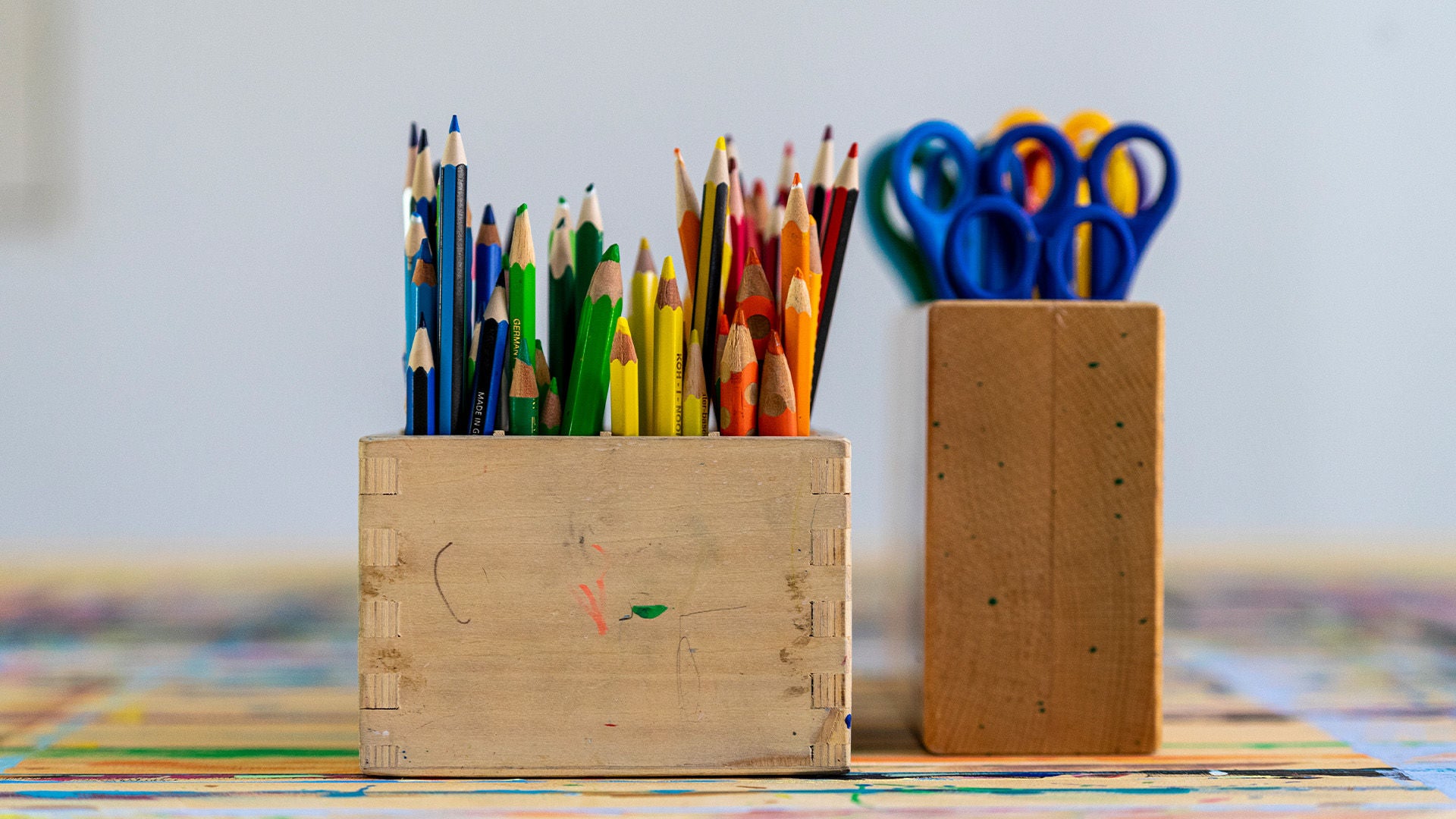 Buntstifte und Bastelequipment, Scheren in verschiedenen Farben, stehen auf einem Tisch bereit.