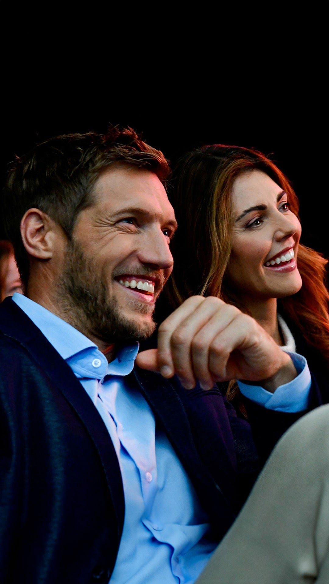 Vier Personen in einem dunklen Raum sitzen nebeneinander und lachen während einer Veranstaltung.