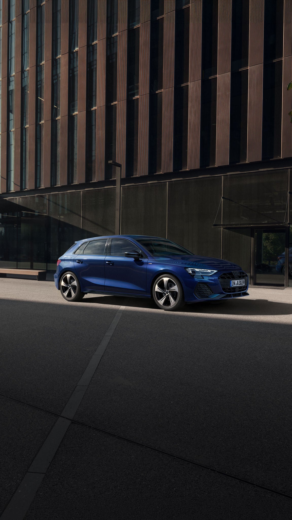 Blauer Audi A3 Sportback vor einem modernen Bürogebäude mit Glasfassade in einem urbanen Umfeld geparkt.