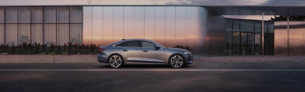 Side view of an silver Audi saloon parked in front of a modern building
