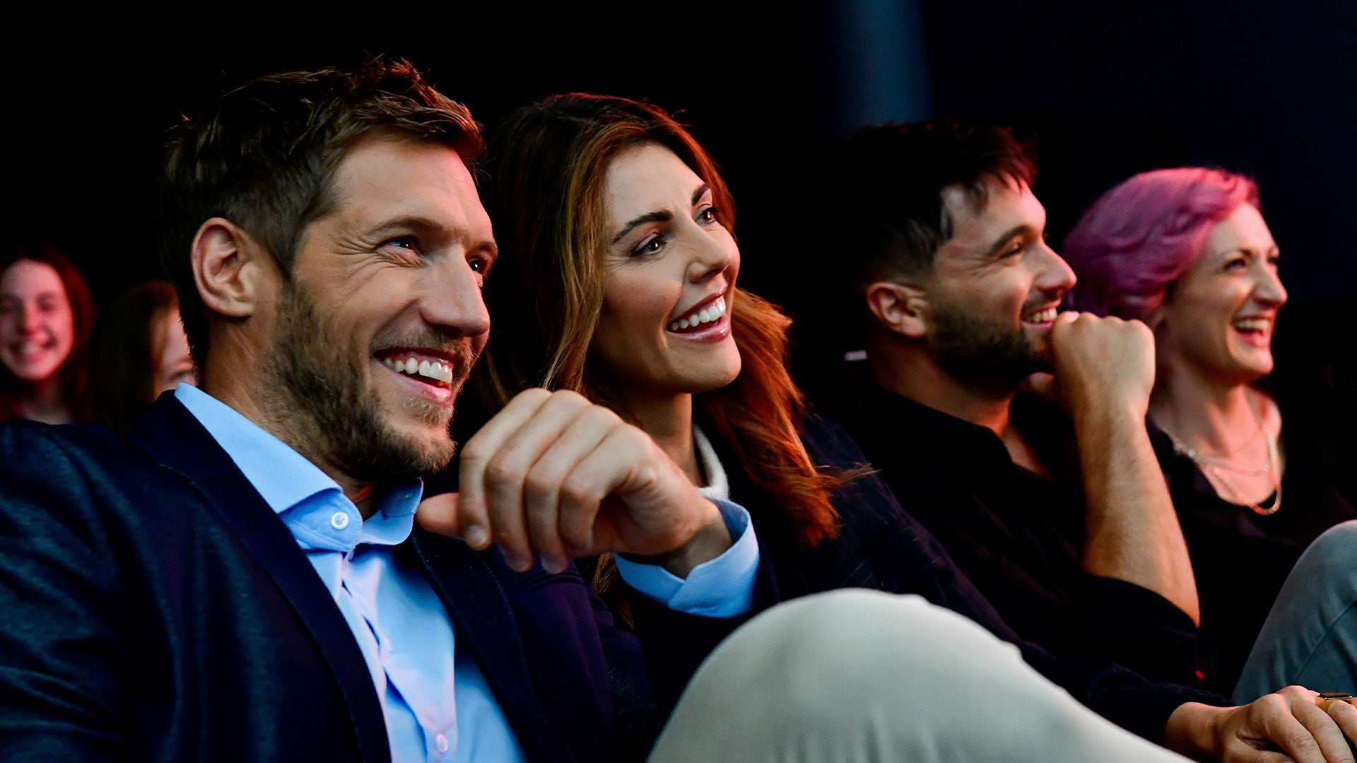 Four people sit next to each other in a dark room and laugh while watching a movie.