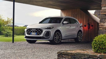 Audi Q5 e-hybrid bianca parcheggiata in una tettoia in legno, collegata a una stazione di ricarica.