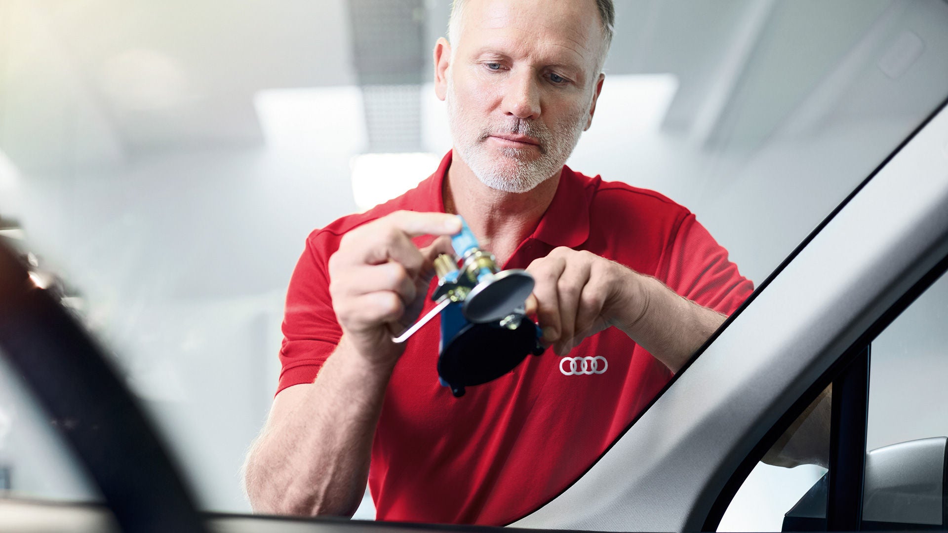 Ein Mitarbeiter im roten Poloshirt testet die Frontscheibe eines Audi.