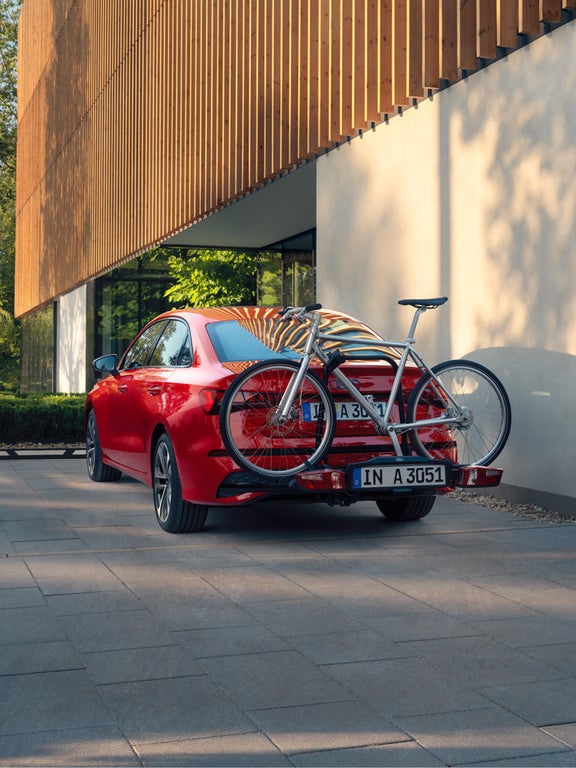 Rote Audi A3 Limousine mit Fahrradträger und silbernem Fahrrad, geparkt vor einem modernen Haus.