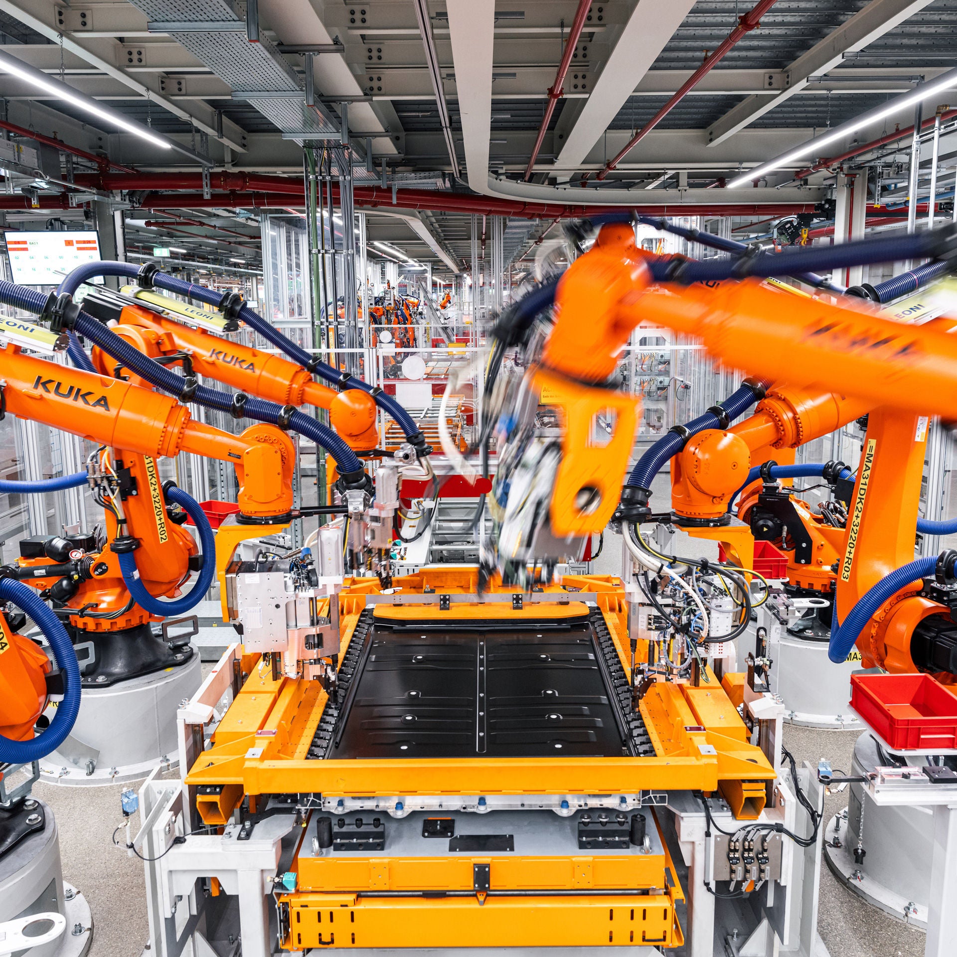 Orange industrial robots automatically assemble a high-voltage battery module in a modern production hall, high-tech and precise.