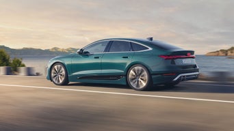 Grüner Audi S6 Sportback e-tron fährt auf einer Straße am Meer entlang, im Hintergrund Küstenlandschaft und sanfte Abendstimmung.