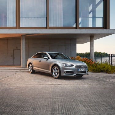 Silver sedan parked in front of a modern house with large windows at dusk.