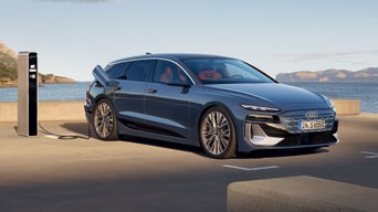 Der S6 Avant e-tron steht rückwärts auf einem Parkplatz und ist dabei an eine Ladestation angeschlossen. Hinter dem Parkplatz sind das Meer und Felsen zu erkennen.