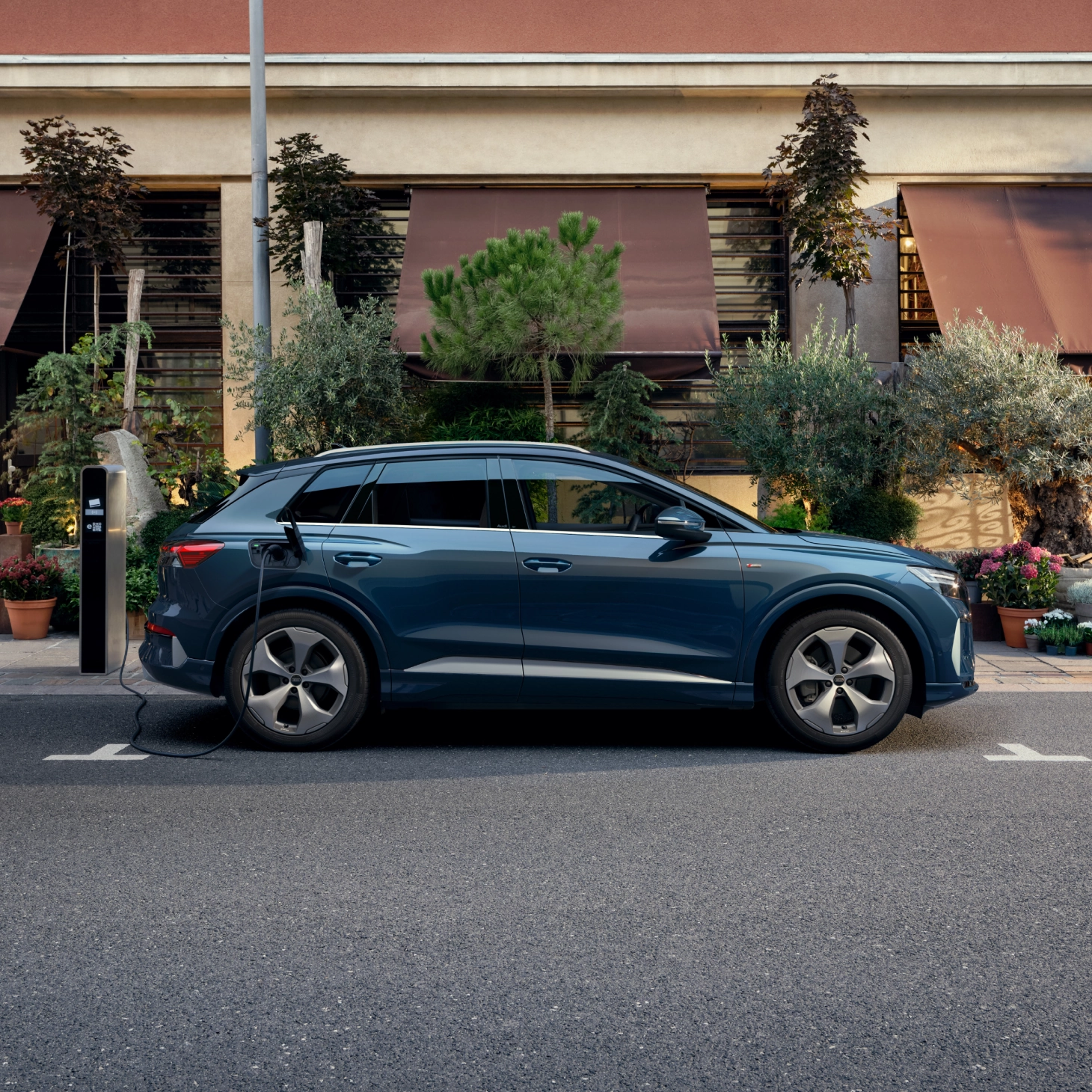 Electric SUV in deep purple, parked at a charging station by a winding road. Mountains and clear sky are visible in the background.