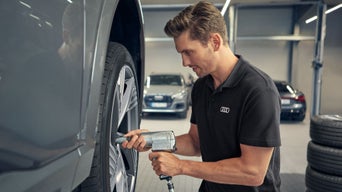 Ein Mann arbeitet in einer Werkstatt an dem Reifen eines Audis auf einer Hebebühne.