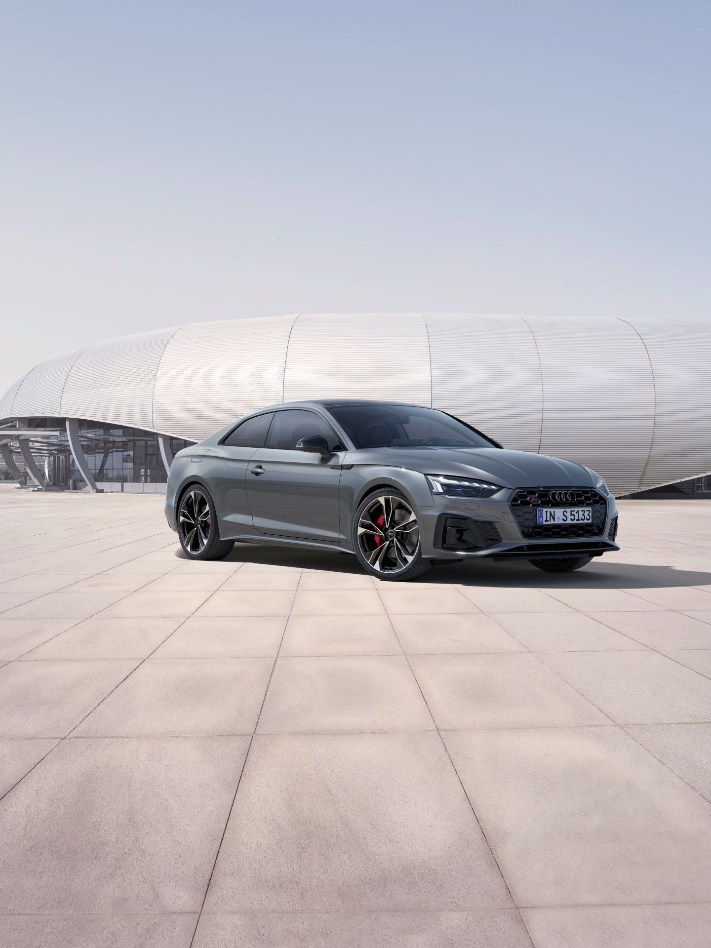 Audi S5 coupe car parked in front of a futuristic building with curved architecture.