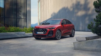 A silver Audi RS e-tron GT drives along a winding road at sunset, with glowing taillights and a mountain backdrop.