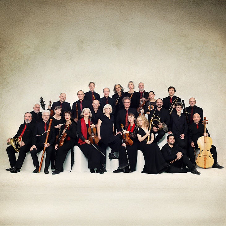 Gruppenfoto der Akademie für Alte Musik Berlin mit historischen Instrumenten vor hellem Hintergrund.