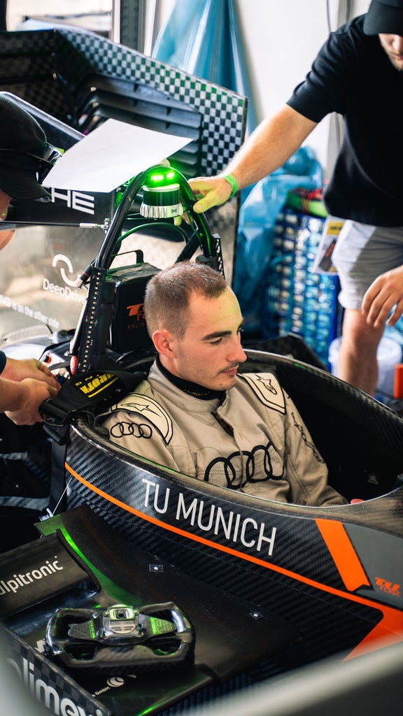 Ein Mann sitzt in einem Rennauto, während zwei andere Personen an dem Auto Arbeiten verrichten