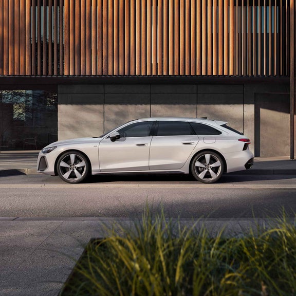 Audi A6 Avant e-hybrid sedd från sidan. Parkerad framför en byggnad i bakgrunden.