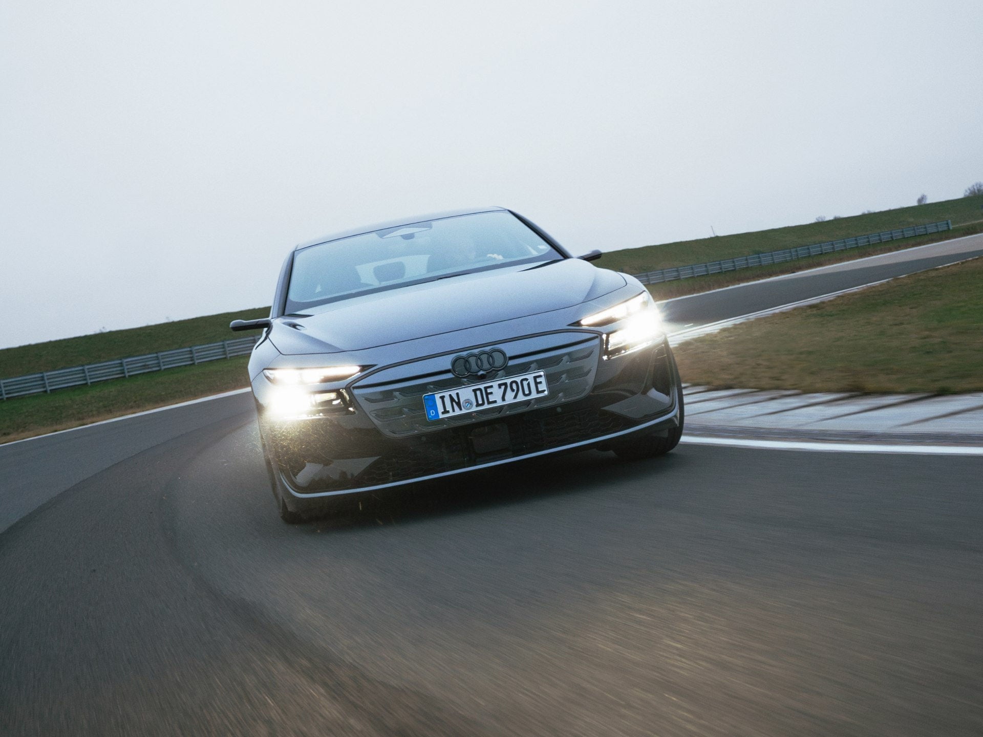 Frontansicht des Audi S6 Avant e-tron. Das Fahrzeug hat eingeschaltete Scheinwerfer und befindet sich in dynamischer Kurvenfahrt auf der asphaltierten Teststrecke der Audi driving experience.