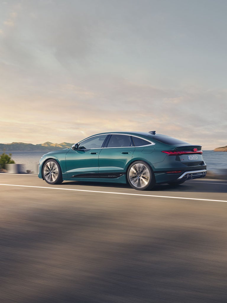 Ein grüner Audi S6 Sportback e-tron fährt auf einer Straße entlang der Küste, Seitenansicht mit Fokus auf die sportliche Silhouette.