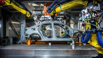 Robot arms assemble an unpainted car body in a production hall.
