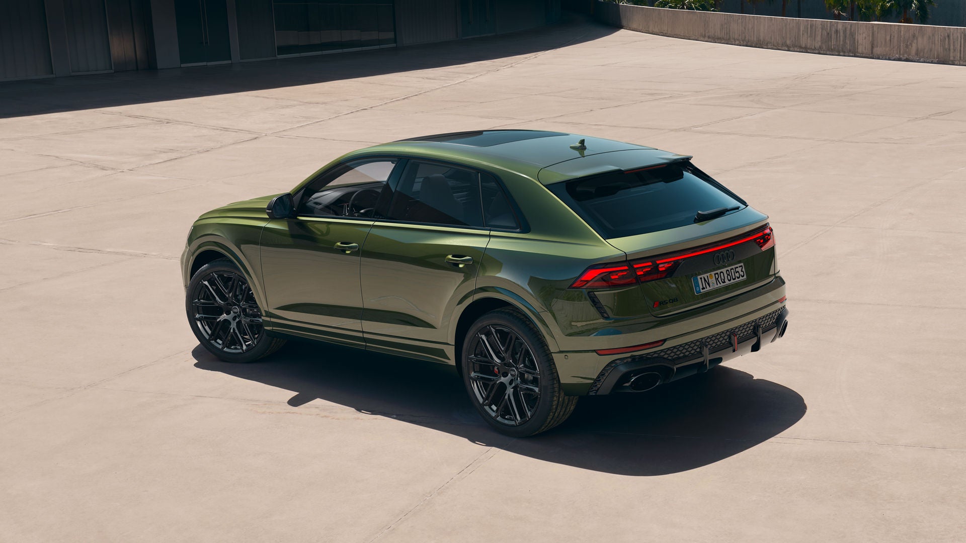 Der RS Q8 SUV von schräg hinten auf einem sonnendurchfluteten Parkplatz vor einem modernen Gebäude.