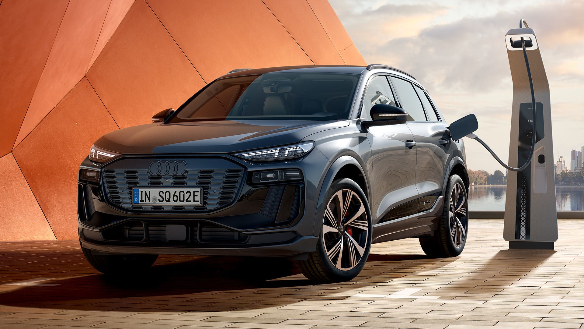 Dunkelgrauer Audi SQ6 e-tron an Ladesäule vor orangefarbener Wand