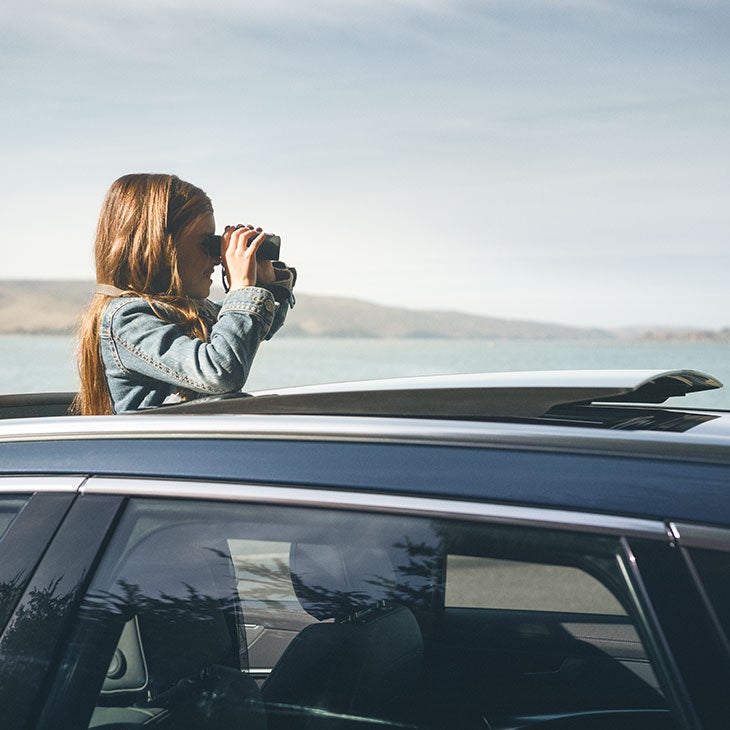 Jente står i takluke på bil og ser utover med kikkert.