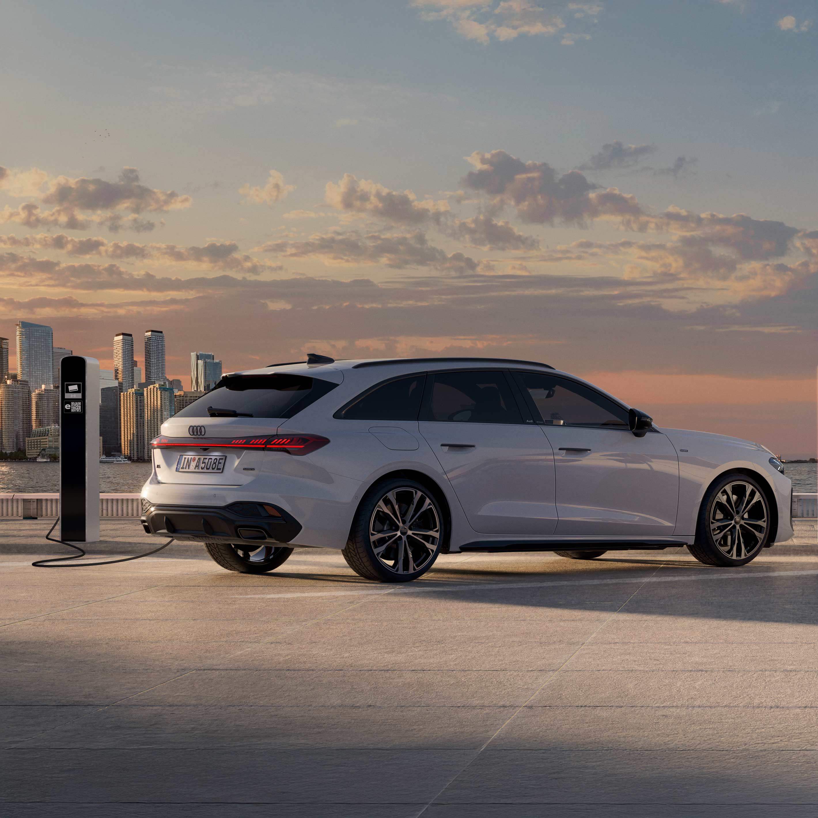Ein weißer Audi A5 Avant e-hybrid beim Laden vor einem See im Licht eines Sonnenuntergangs