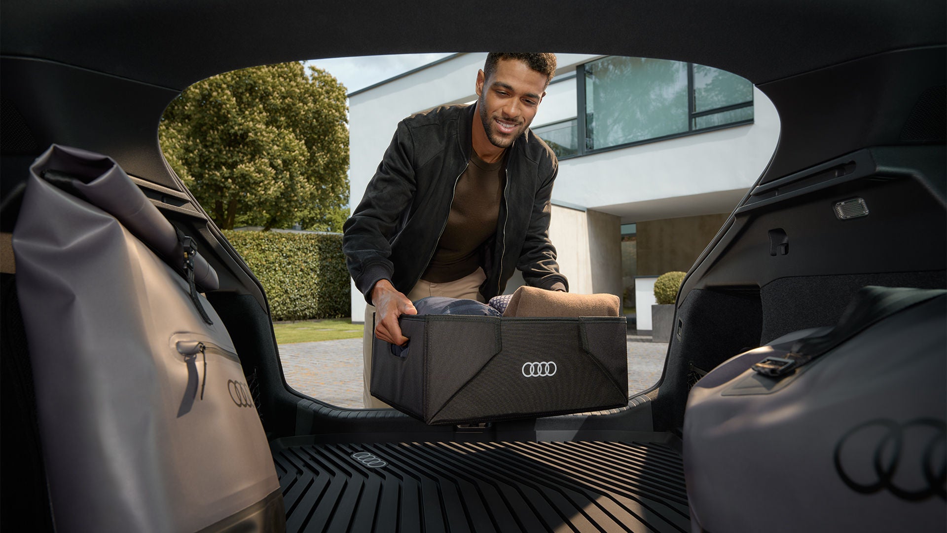 Un homme charge le coffre d’un Audi avec une boîte d’organisation Audi pliable, flanquée de sacs de voyage Audi assortis.