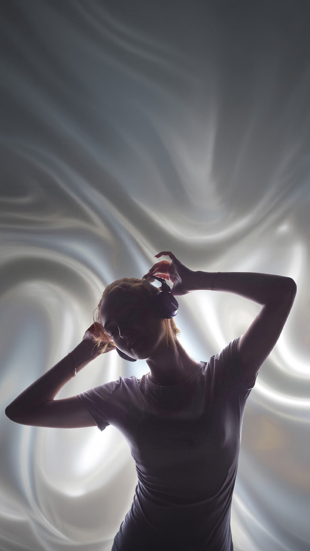 Person mit Kopfhörern im Profil hebt die Hände an den Kopfhörer, vor hellem, weich verschwommenem Hintergrund.