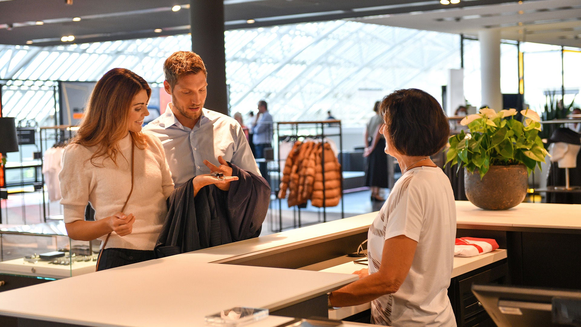 Couple stands at a modern shop counter speaking to a saleswoman.  