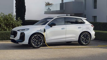 Side profile of a white Q3 SUV e-hybrid charging in the parking lot in front of a modern house.