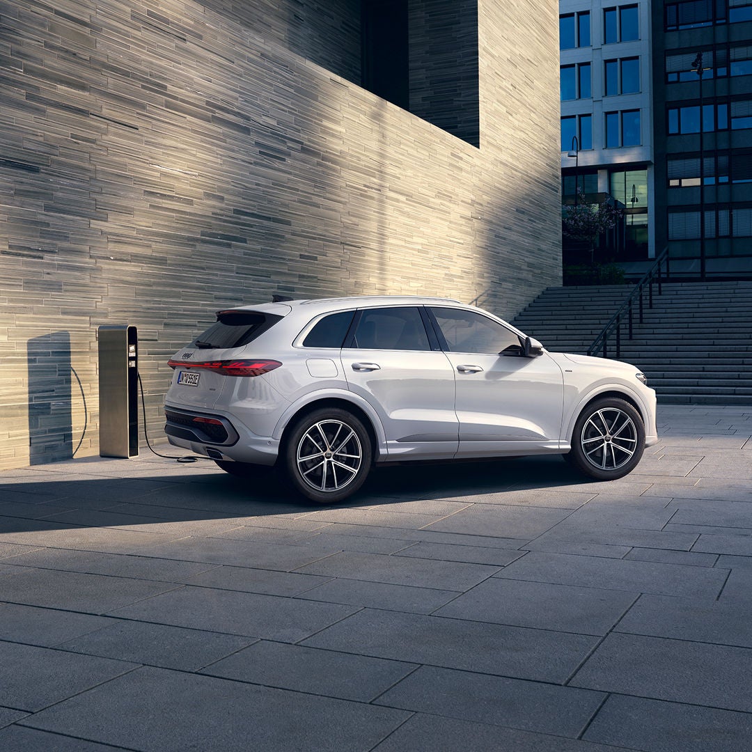Silver SUV charging at a modern electric station, set against a backdrop of sleek, urban architecture and steps, conveying innovation and sustainability.