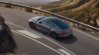 A grey Audi driving on a highway with mountainous scenery in the background.