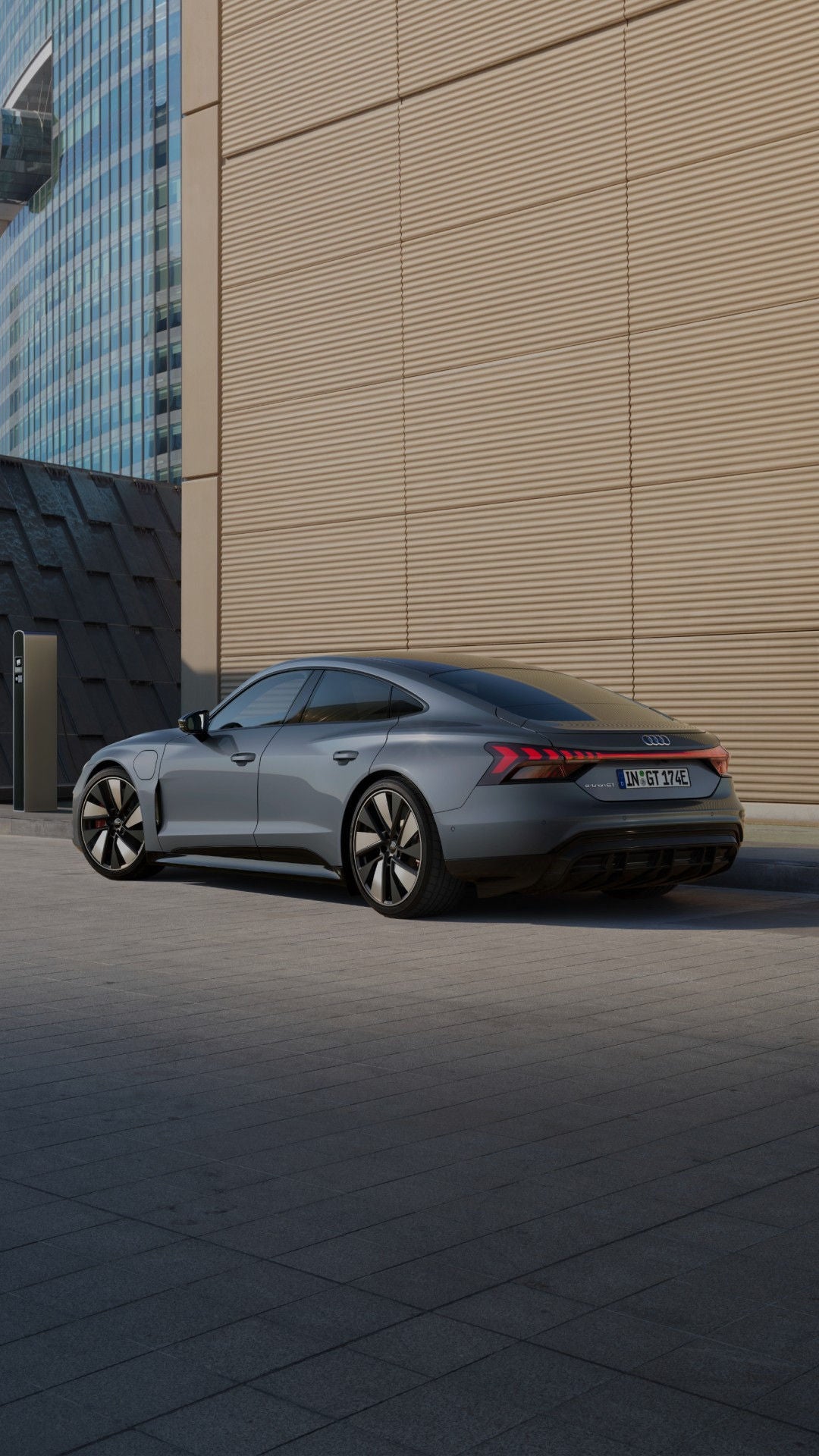 An electric Audi car is parked beside a sleek, futuristic building. A woman in a stylish teal outfit walks confidently.